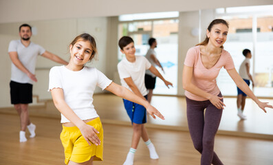 Fototapeta premium Portrait of positive pre-teen girl doing dance workout with her brother and parents during family class