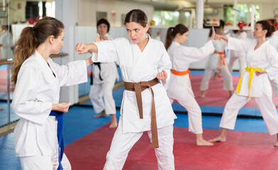 European women practice kicks and punches in self-defense training. Women in white kimono trying...