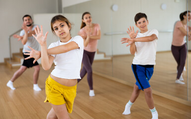 Happy sporty family of four enjoying active dance in modern studio. Focus on smiling brunette...