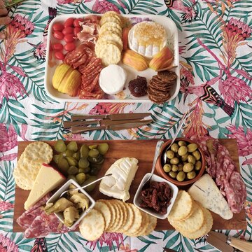 Abundant homemade cheeseboard for a family celebration. There is an assortment of cheeses and cold cuts on inviting platters. They are served on a bright tablecloth