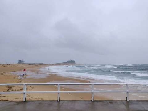 View of Newcaslte Beach, NSW, with waves behind a fence on a stormy day