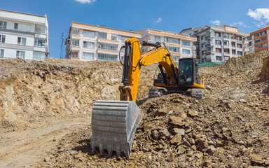 Excavator at urban construction site with residential buildings behind