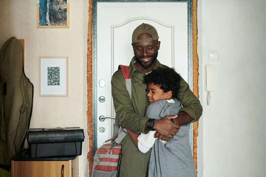 African American man hugging happy child in cozy home entrance hallway, creating heartwarming moment of reunion