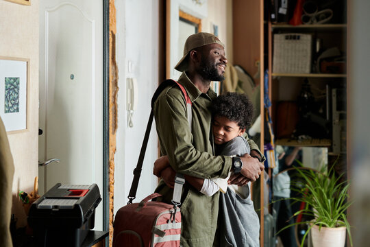 An African American man embracing child inside cozy home, surrounded by household items and decorations. Heartwarming bond displayed in warm interior setting