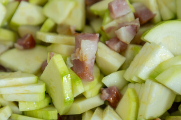 Chopped zucchini and bacon cooking in a frying pan close up

