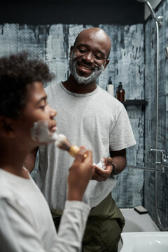Smiling father showing young boy how to shave in bathroom giving hands-on experience creating bonding moment