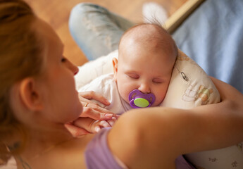 young mother holding sleeping newborn baby on her lap at home