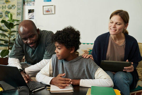 Family exploring educational resources together on laptop in comfortable home setting. Child closely observing information on screen, parents assisting and discussing content