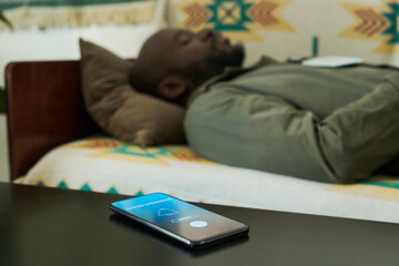 African American man resting on patterned couch with mobile phone placed on table in foreground