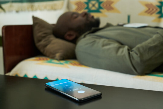 African American man resting on patterned couch with mobile phone placed on table in foreground