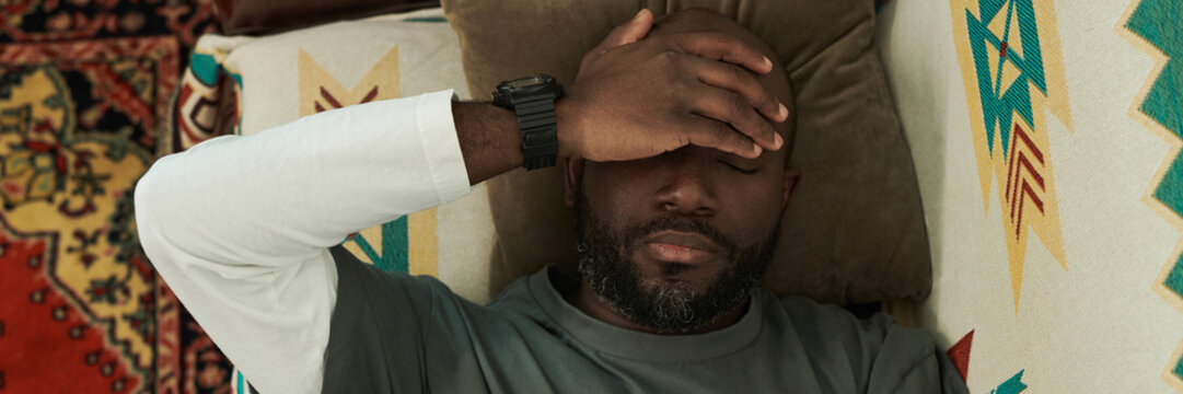 Resting Man Lying on Couch with Hand Over His Forehead Header