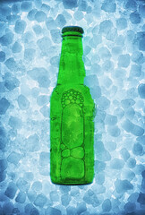 Green beer bottle buried on pile of ice cubes backlit