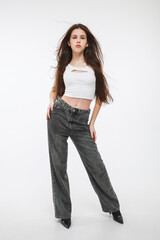 A brunette girl in a white top and gray jeans on a white background.