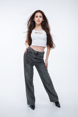 A brunette girl in a white top and gray jeans on a white background.
