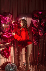valentine's day party. young girl with slim legs in red fur is standing fashion in profile with smile on a pink background with hearts balloons and disco balls on floor. lifestyle concept, free space