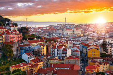 Lisbon, Portugal. Top view panorama of sunset. Evening picturesque scene at houses in historic old town in district Alfama. 25th April Bridge far away. Sky with dramatic clouds and sun.
