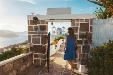Young woman tourist in blue dress standing at open doors with view of sea and church on Milos island, Greece. Travel concept. Picturesque views of Milos island in Greece