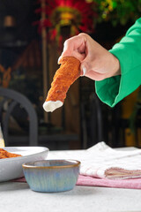 Chef dipping breaded chicken finger in creamy sauce: restaurant scene