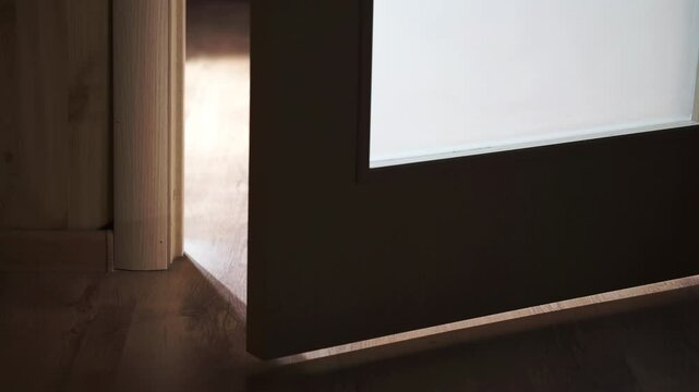 Door slowly opens and closes. Door opens from a dark hallway into a lighted room. Light shines from door opening in dark room