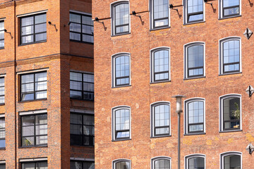 Historic red brick industrial building with large windows in an urban environment. Industrial style architecture with modern renovations under a clear sky