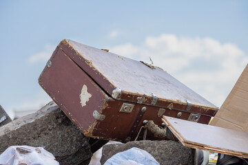 A large trash container filled with plastic bags, cardboard boxes and an old suitcase. An overflowing trash container with various waste and discarded items