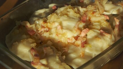 Polish pierogi with fried onion and bacon – traditional homemade dumplings in glass tray, captured in warm sunlight, close-up