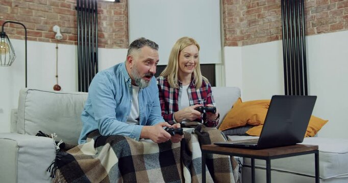 Woman celebrating victory when playing video game together with her excited bearded husband during family leisure at home