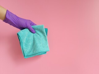Girl's hand in purple rubber protective glove holds colored rags on pink background