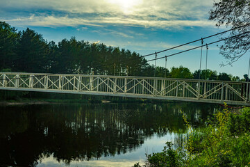 Fototapeta premium Suspension Bridge Over Calm River Under Cloudy Sky