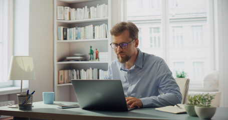 Fototapeta premium Creative Man Works on His Laptop at a Desk. Professional Marketing Writer Deep in Thought, Analysis and Creative Process, Focused and Creative Workspace. Starting Work