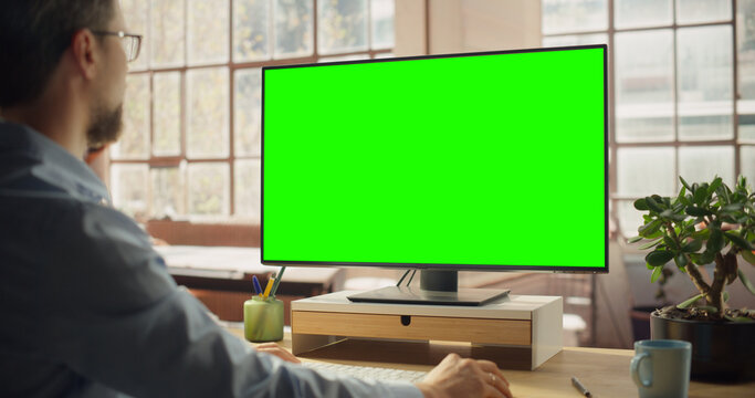 Professional Black Female Using Green Screen Monitor for Content Creation. Creative working on Chroma Key Display. Modern Home Office with Minimalist Interior. Over the Shoulder Shot