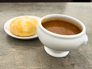 Hearty tomato soup with bread roll on rustic table