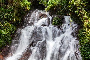 Closeup, Jembong waterfall, Nothern Bali, Indonesia. Water cascading over rocks; lush green vegetation on both sides. 

