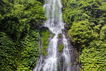 Closeup of Sekumpul waterfall, northern Bali, Indonesia. Water cascading over rocks; lush green vegetation on the cliff at either side. 
