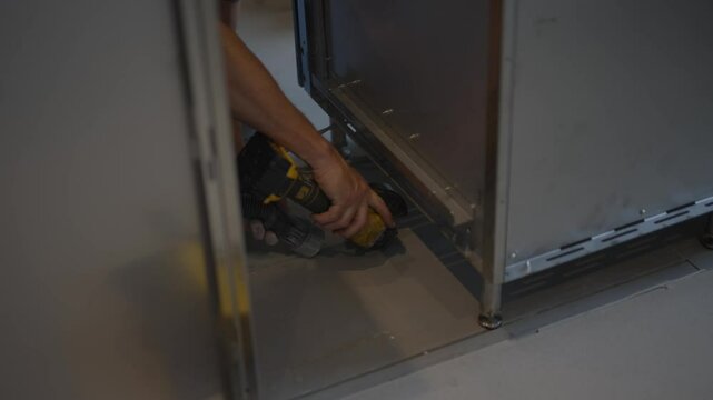 A man is using a drill to open a door. The door is made of metal and is located in a room
