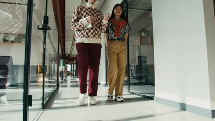 Low section full shot of Caucasian male and Chinese female social media managers discussing new content plan for client while walking along corridor in coworking space