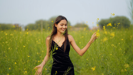 Indian happy young adult gen z model woman lady wear black dress standing outdoor enjoy nature...