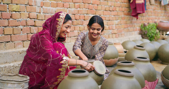 Indian mature adult woman lady mother with young teen middle age girl sitting home making hand made potters shape touches clay pots asian female art skill create pottery mud product outside house - Powered by Adobe