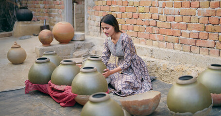 Indian teenage village woman wear casual dress sitting outdoor making hand made potters finishing...