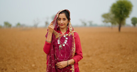 Indian mature adult gen x village farmer woman wear red saree standing outdoor farmland looking at...