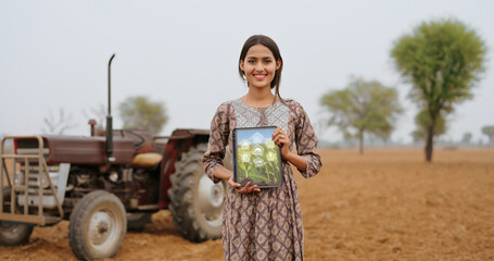 Indian young adult gen z farmer woman lady wear casual dress standing outdoor farmland hold green screen tablet device look at camera Asian smiling teen age girl do pose staring cam outside desi life