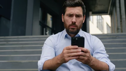 Gordijnen Stressed unemployed fired business man with dismissal box chatting phone searching new job online service dismiss businessman upset in city financial crisis holding smartphone near office building © Yuliia