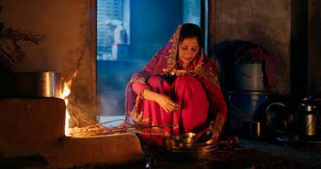 Indian villager gen x woman preparing food using traditional earthen mud stove indoor house asian...