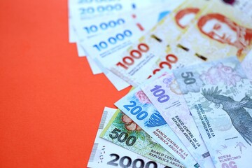 Argentine pesos money bills in big amount lies on red color table close up