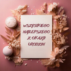 kartka lub baner z życzeniami urodzinowymi w kolorze różowym w białym prostokącie i wokół suszonych kwiatów świeca w odcieniach różu, beżu i bieli na różowym tle gradientowym