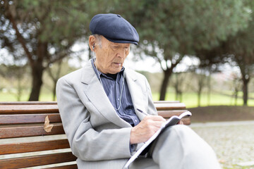 Obraz premium Elderly man writing notes while listening music on park bench