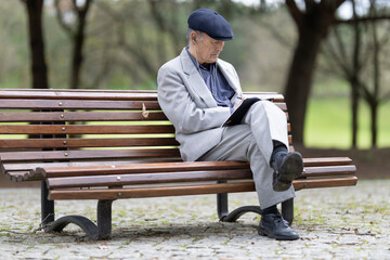 Fototapeta premium Senior professor writing notes while sitting on bench in park
