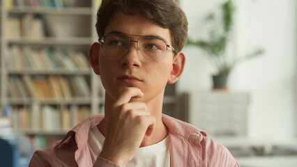 Fototapeta premium Close up portrait Caucasian teenager guy pensive looking around thinking ponder choosing book in school college academy university library man teen boy think thoughtful education studying concept