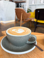 A steaming cappuccino rests on a rustic wooden table in a stylish café, its creamy foam art contrasting with sleek contemporary interiors. Perfect for coffee brands and café lifestyle content.