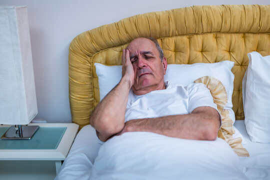 Worried senior man having a headache after waking up in bed during early morning hours. - Powered by Adobe